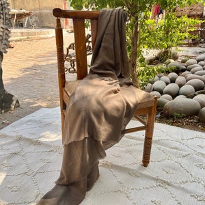 May include: A brown throw blanket draped over a wooden chair with a carved back and turned legs. The chair is sitting on a white rug with a diamond pattern.