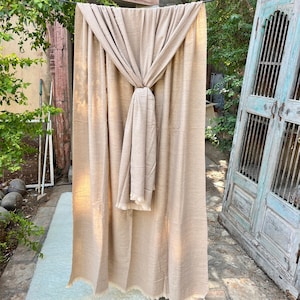 May include: A light brown pashmina shawl with a fringed edge. The shawl is draped over a chair and tied in a knot at the front.