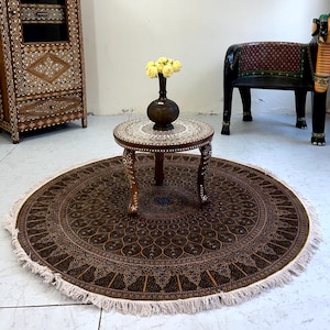 May include: An interior scene featuring a round, patterned rug with a fringed edge, a small decorative table, and a cabinet. A framed portrait hangs on the wall, and a decorative elephant-shaped chair is also present. The room has a vintage aesthetic.