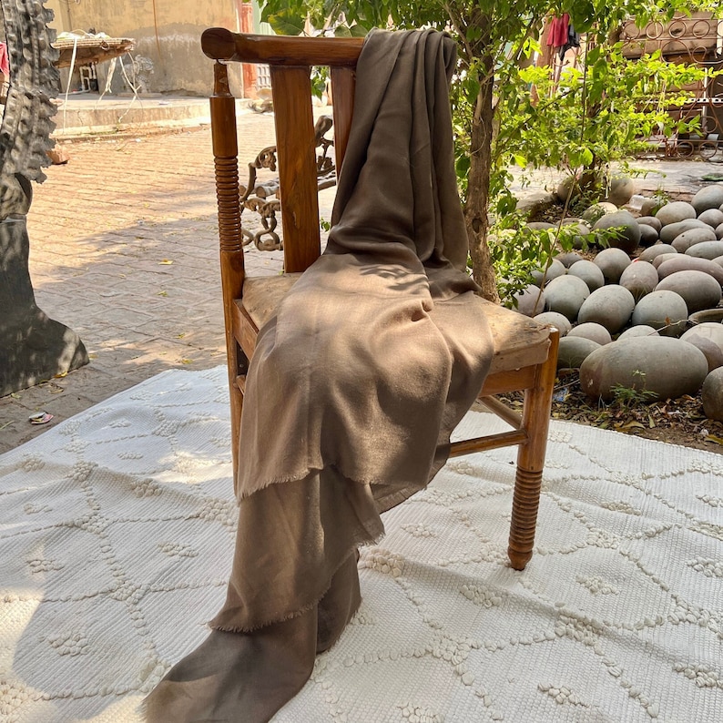 May include: A brown throw blanket draped over a wooden chair with a carved back and turned legs. The chair is sitting on a white rug with a diamond pattern.