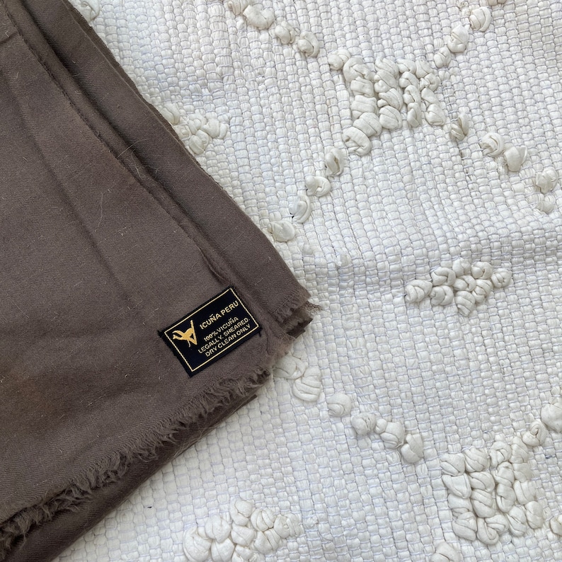 May include: A brown alpaca wool throw blanket with a label that reads "Icu&ntilde;a Peru 100% Alpaca Legally Sheared Dry Clean Only".