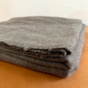 Puede incluir: Una manta de lana gris doblada con una superficie suave y texturizada.