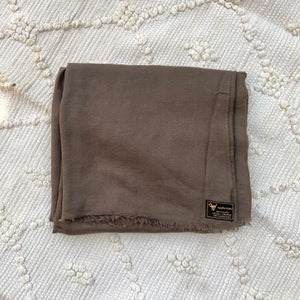 May include: A brown linen scarf with a frayed edge and a small black label that reads "Victoria Peru 100% Viscose Eco-Friendly Locally Woven & Dyed in Peru".