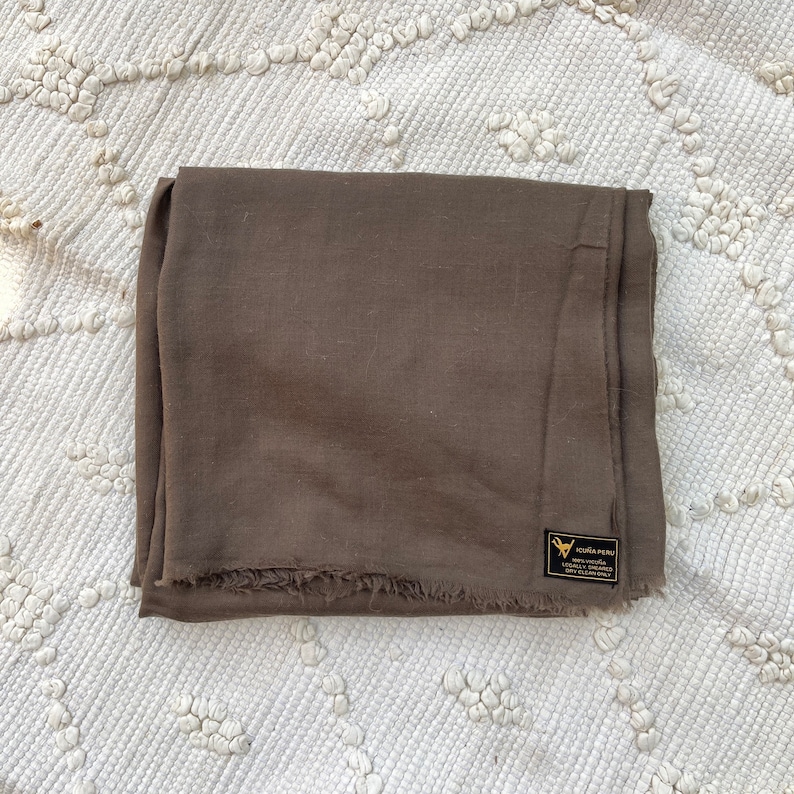 May include: A brown linen scarf with a frayed edge and a small black label that reads "Victoria Peru 100% Viscose Eco-Friendly Locally Woven & Dyed in Peru".