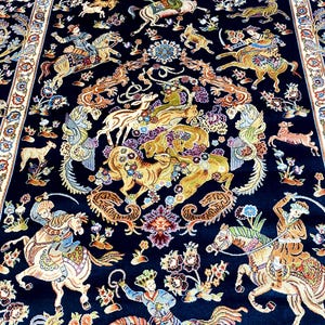 May include: A detailed, hand-knotted rug with a dark blue background. The rug features a complex design of riders on horseback, deer, and floral patterns in shades of gold, cream, and various colors.