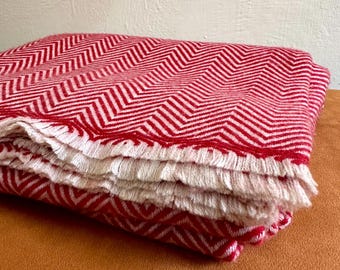 May include: A red and white chevron patterned throw blanket folded on a brown surface. The blanket has a fringe border.
