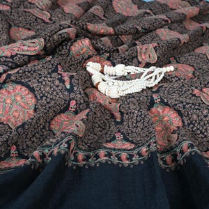 May include: A black shawl with intricate paisley patterns in shades of pink, brown, and green. A white beaded necklace is draped across the shawl.