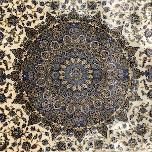 May include: An ornate, cream-colored rug with a central medallion design in shades of blue, brown, and gold. The medallion is surrounded by a floral pattern, and the rug has a detailed, textured appearance. The overall design is symmetrical and intricate.