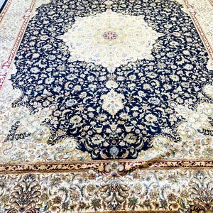 May include: Large, ornate area rug with a central medallion design. The rug features a cream-colored center surrounded by a navy blue border filled with floral patterns. The border is trimmed with gold and red accents, and the rug has a fringed edge.