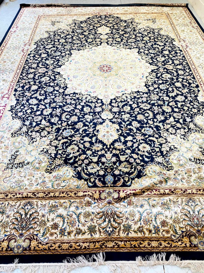 May include: Large, ornate area rug with a central medallion design. The rug features a cream-colored center surrounded by a navy blue border filled with floral patterns. The border is trimmed with gold and red accents, and the rug has a fringed edge.