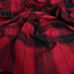 Puede incluir: Tela de cuadros rojos y negros con un tacto suave y texturado. La tela está doblada y drapeada, mostrando el patrón y la textura.