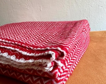 May include: A red and white chevron patterned throw blanket folded on a brown surface.