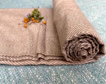 Könnte beinhalten: Eine braune und weiße Decke mit Fischgrätenmuster, die auf einer blauen, strukturierten Oberfläche aufgerollt ist.