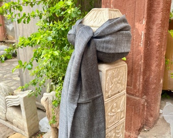 May include: A grey scarf draped over a stone pillar with intricate carvings. The scarf is made of a soft, textured fabric and has a simple, elegant design.