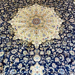 May include: An ornate, navy blue area rug with a central medallion design. The rug features a cream-colored center with intricate floral patterns in shades of gold, blue, and green. The border is a deep navy blue, also adorned with floral motifs.