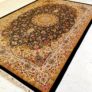 May include: A rectangular, ornate rug with a black central field and a detailed floral pattern in shades of gold, red, and blue. The border is cream-colored with a repeating floral design, and the rug has a black edge and fringe.