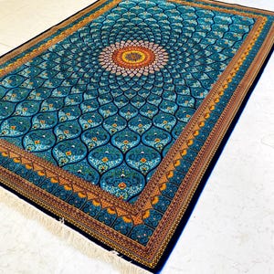 May include: A rectangular, ornate rug with a central medallion design. The rug features a teal background with a repeating pattern of stylized floral motifs in shades of blue, orange, and white. The border is a dark blue with an intricate design and fringe.