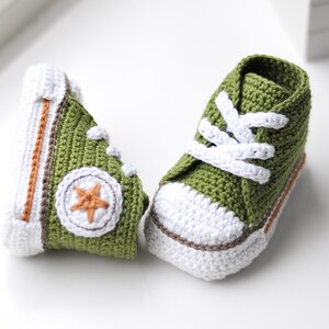 以下が含まれることがあります： 白のレースと側面に白い星が付いた緑色の編み物のベビーシューズのペアです。