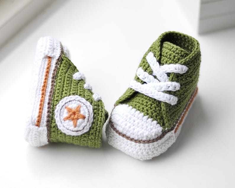 以下が含まれることがあります： 白のレースと側面に白い星が付いた緑色の編み物のベビーシューズのペアです。