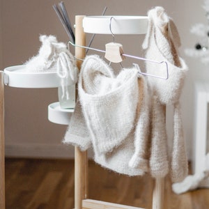 Pode incluir: Um cabide de madeira branco com duas prateleiras brancas e um cabide de metal. Dois su&eacute;teres de malha branca est&atilde;o pendurados no cabide.