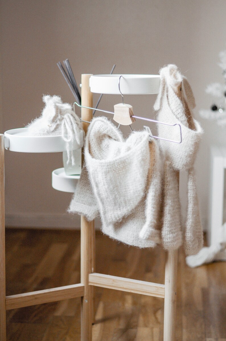 Pode incluir: Um cabide de madeira branco com duas prateleiras brancas e um cabide de metal. Dois su&eacute;teres de malha branca est&atilde;o pendurados no cabide.