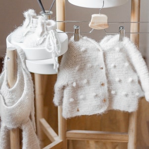 Pode incluir: Um casaco branco de croch&ecirc; com fecho de bot&atilde;o e um chap&eacute;u e botinhas brancas de croch&ecirc;.