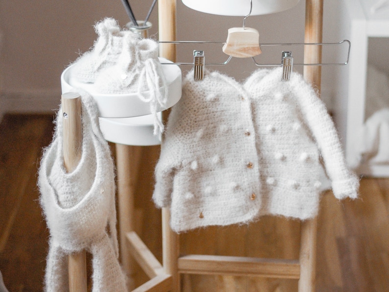 Pode incluir: Um casaco branco de croch&ecirc; com fecho de bot&atilde;o e um chap&eacute;u e botinhas brancas de croch&ecirc;.