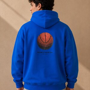 May include: A royal blue hoodie featuring a basketball graphic on the back. The basketball is orange and brown with black lines. The text "BARNEYS NEWYORK EST. 1923" is printed below the basketball. The hoodie has a hood and long sleeves.