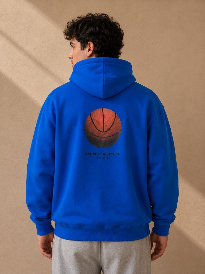 May include: A royal blue hoodie featuring a basketball graphic on the back. The basketball is orange and brown with black lines. The text "BARNEYS NEWYORK EST. 1923" is printed below the basketball. The hoodie has a hood and long sleeves.