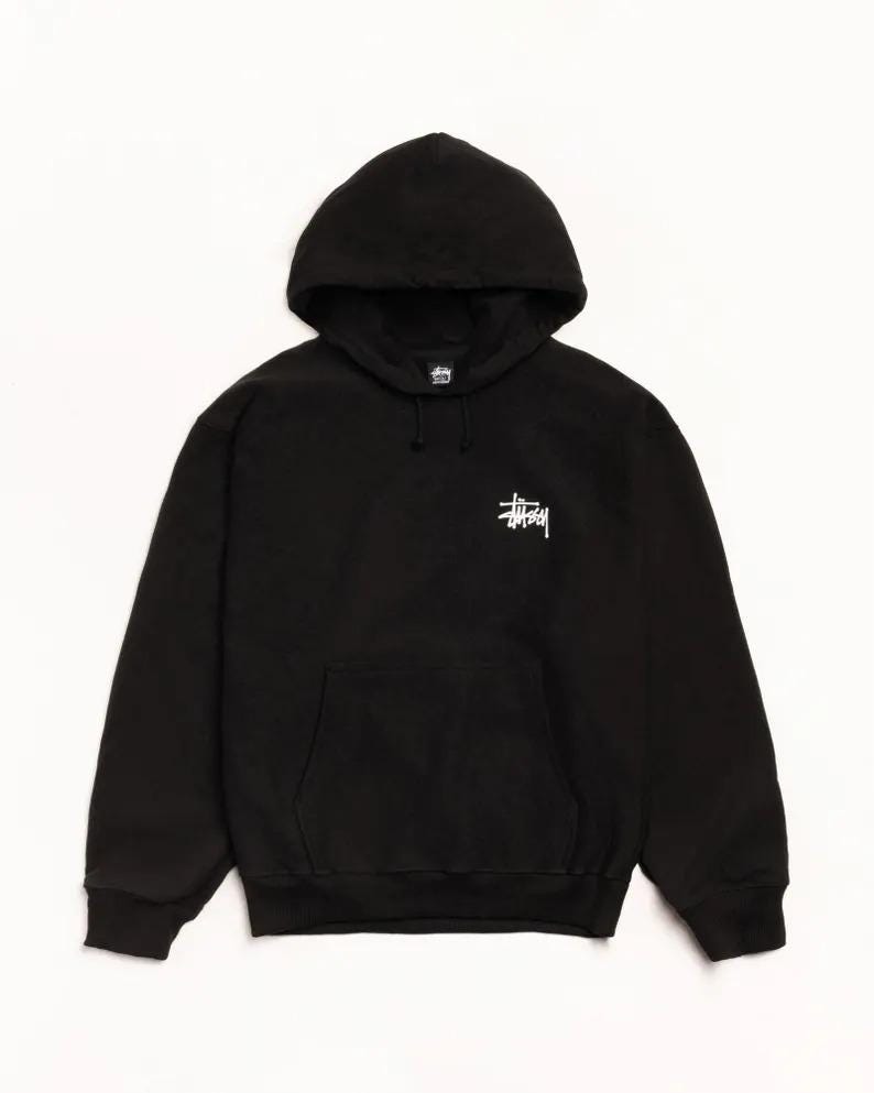 May include: Black hooded sweatshirt with a kangaroo pocket and white logo on the chest. The sweatshirt has a drawstring hood and ribbed cuffs and hem. The logo is a stylized, white graphic.