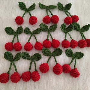 Puede incluir: Una colección de 18 adornos de cereza de ganchillo con hojas verdes. Las cerezas son rojas y las hojas son verdes.
