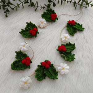 Può includere: Una ghirlanda natalizia fatta a mano con foglie di agrifoglio verdi all'uncinetto con bacche rosse e fiori bianchi infilati su uno spago naturale. Perfetta per le decorazioni natalizie.