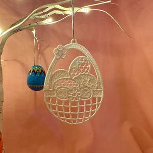 May include: White crocheted Easter egg ornament shaped like a basket with a floral design and eggs inside.