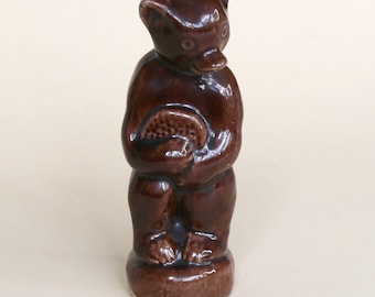May include: A brown ceramic figurine of a bear holding a honeycomb. The bear is standing on a round base.
