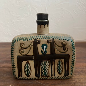 Op de afbeelding: Een keramische fles met een bruin en groen ontwerp van twee gestileerde paarden. De fles heeft een rechthoekige vorm met een afgeronde bovenkant en een bruine kurk.