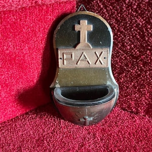 May include: A vintage wall-mounted holy water font with a cross at the top and the word "PAX" below. The font is made of metal with a dark brown and bronze finish. The font has a small basin at the bottom.
