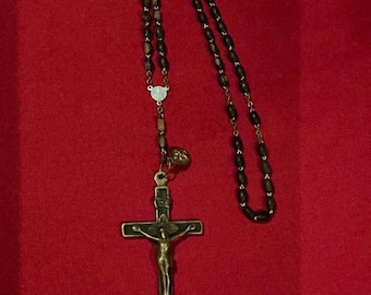 May include: A rosary with dark wooden beads and a metal crucifix. The crucifix features a detailed depiction of Jesus Christ. The rosary is displayed against a red background.