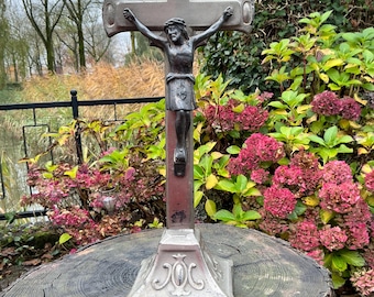 May include: A silver metal crucifix with a figure of Jesus Christ on the cross. The crucifix is standing on a wooden stump with a base that reads "69900000".