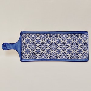 Pode incluir: Uma bandeja de servir de cerâmica azul e branca com um padrão floral decorativo. A bandeja tem uma alça de um lado.