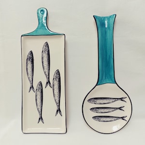 Könnte beinhalten: Zwei Keramik-Servierplatten mit blau-weißem Design. Eine Platte ist ein rechteckiges Serviertablett mit schwarzem Rand und vier Fischillustrationen. Die andere Platte ist ein Löffelabstellplatz mit blauem Griff und einer weißen Schale mit vier Fischillustrationen.