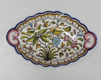 May include: A white ceramic serving dish with pink handles. The dish is decorated with a floral pattern in shades of blue, yellow, green, and pink. A small bird is perched on a branch in the center of the design.