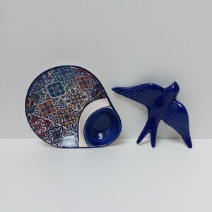May include: A blue and white ceramic dish with a decorative pattern and a small blue bowl. A blue ceramic swallow figurine is also pictured.