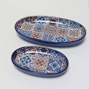 Op de afbeelding: Twee ovale serveerschalen van keramiek met een blauwe rand en een kleurrijk geometrisch patroon. Het patroon heeft blauwe, oranje en witte tegels.