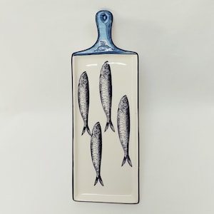Op de afbeelding: Witte keramische serveerschaal met een blauwe handgreep en een zwart-witte illustratie van vijf vissen.