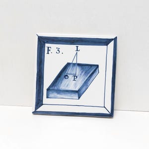 Può includere: Una piastrella di ceramica blu e bianca con una cornice blu. La piastrella presenta un prisma rettangolare blu con le lettere "O" e "P" sulla superficie superiore. Una linea blu si estende dalla cima del prisma fino alla lettera "L" sopra di essa. Il testo "F.3." si trova nell'angolo in alto a sinistra della piastrella.