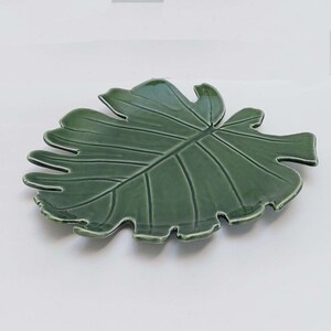 May include: A green ceramic leaf-shaped serving dish. The dish is designed to look like a large tropical leaf.