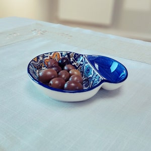 May include: A blue and white ceramic serving dish with a divided section. The dish is decorated with a floral pattern and has a glossy finish. The dish is filled with olives.