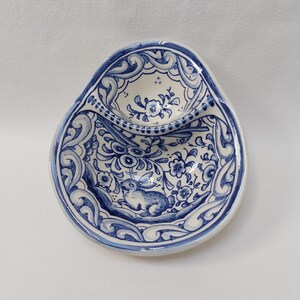 May include: Oval-shaped ceramic dish with a blue and white floral design. The dish features a small, raised compartment and a detailed border. A blue rabbit is painted on the bottom of the dish.