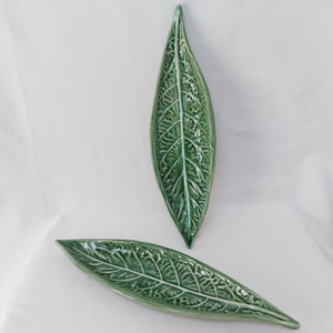 Peut inclure: Deux plats de service en céramique en forme de feuille verte. Les plats sont conçus pour ressembler à de vraies feuilles avec des nervures et une surface texturée.