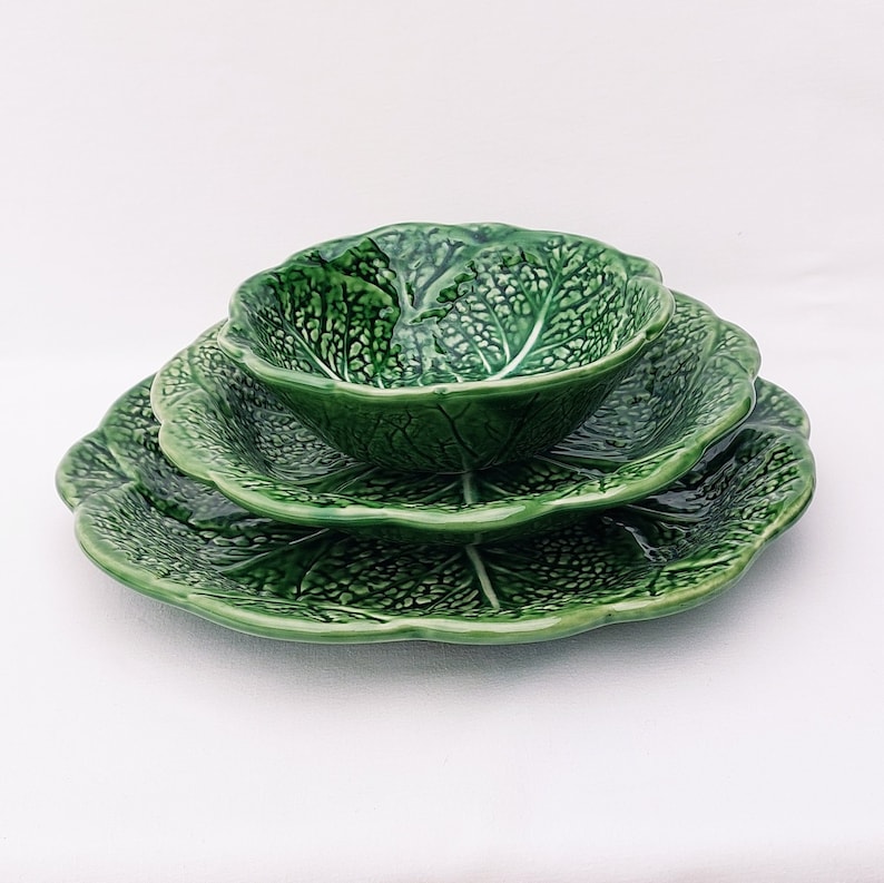 May include: A set of three green ceramic bowls shaped like cabbage leaves. The bowls are nested together, with the smallest bowl on top.